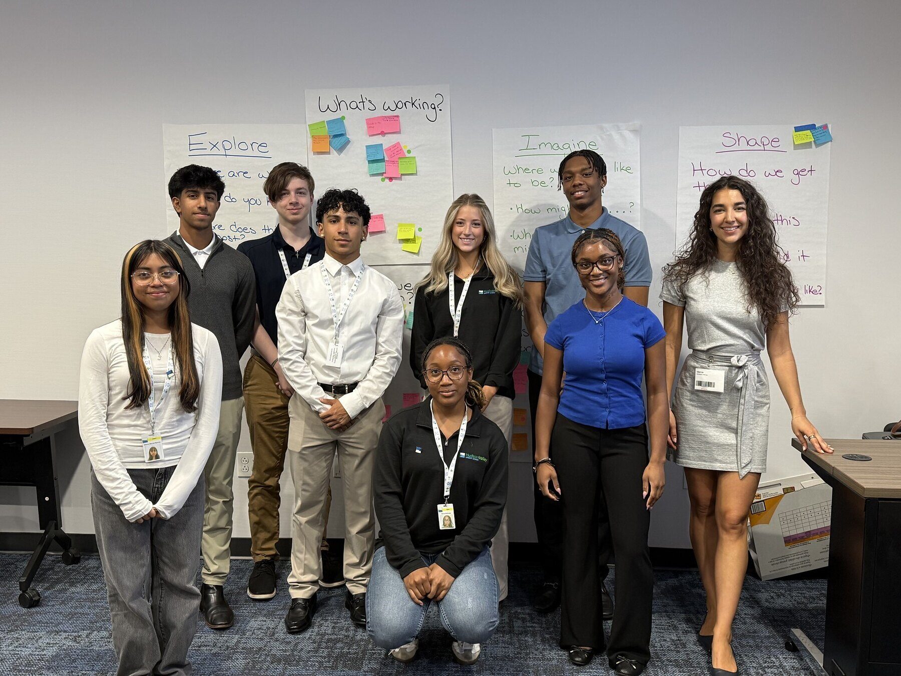 Mikhaila Ackerbauer with the nine Hudson Valley Credit Union interns in front of the Explore, Imagine and Shape charts